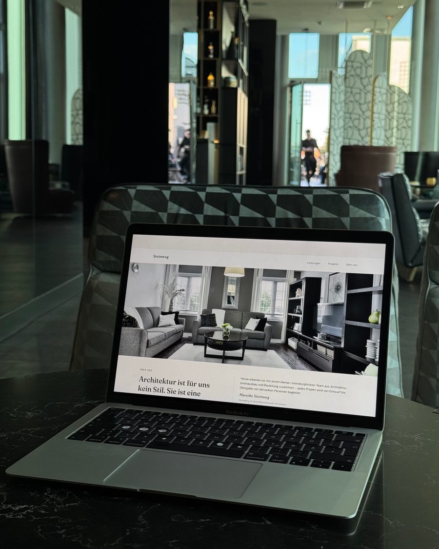 Aufgeklappter Laptop mit einer Website auf dem Bildschirm, im Hintergrund eine helle Lobby